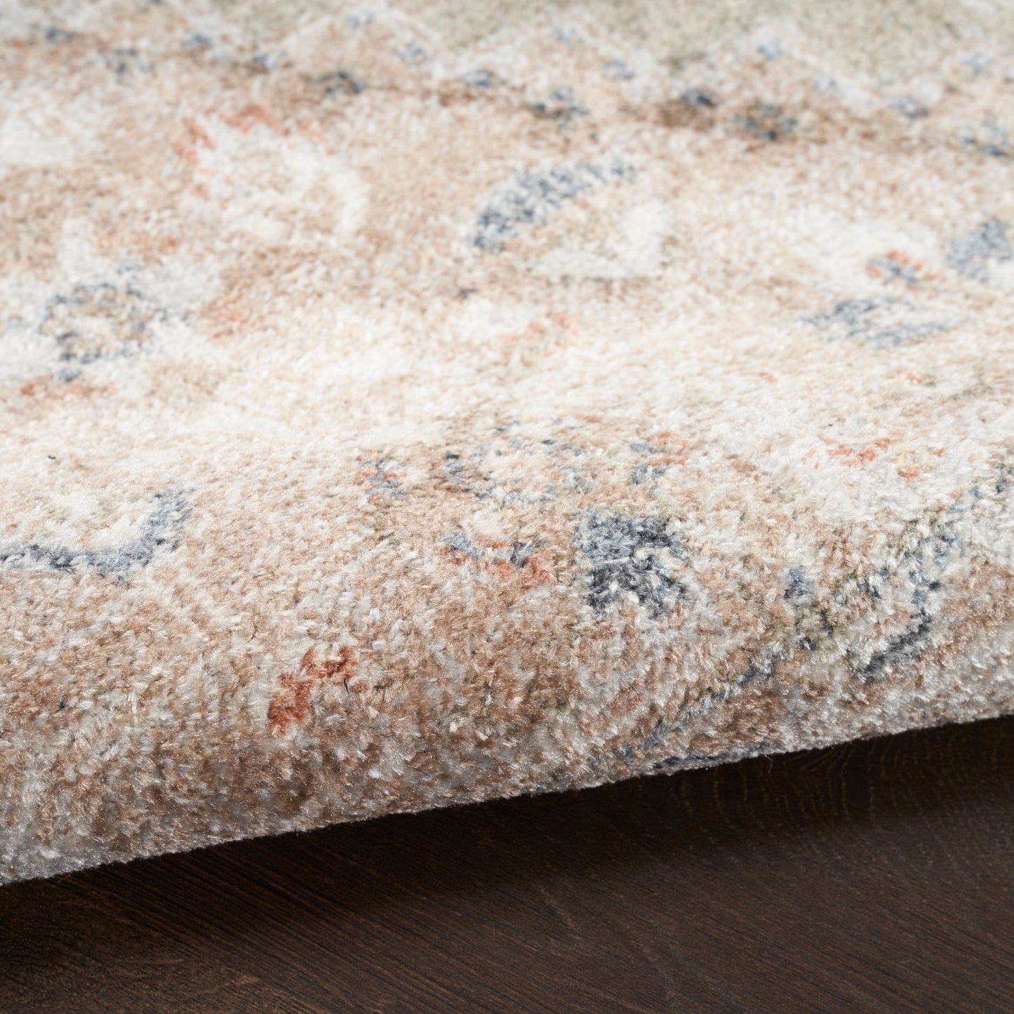 Beige patterned round area rug (5' diameter) with soft pile and blue, orange, gray floral motifs on dark wood floor.