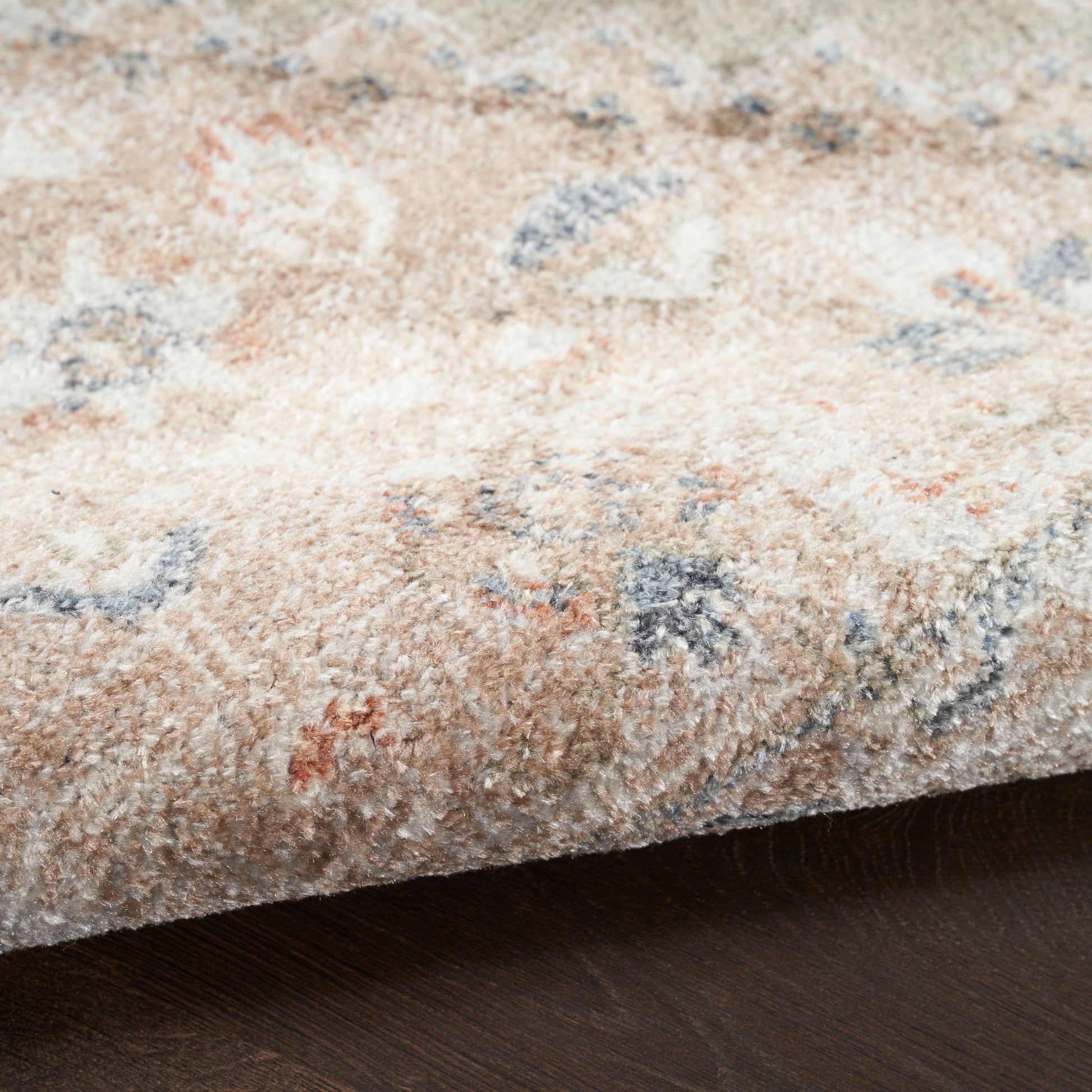 Beige patterned round area rug (5' diameter) with soft pile and blue, orange, gray floral motifs on dark wood floor.