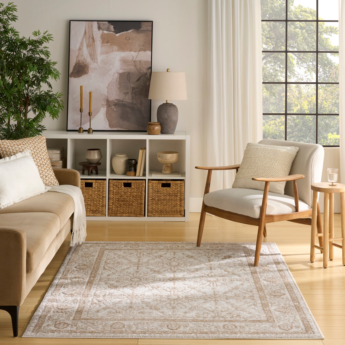 Neutral living room with beige sofa, midcentury armchair, woven baskets, large abstract art, greenery, and sunlit window.