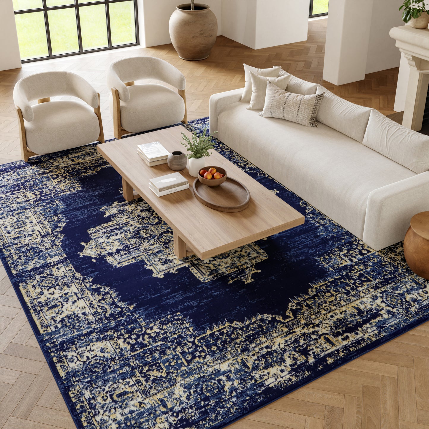 Navy distressed rug on a living room floor with a beige sofa, two cream armchairs, and a light wood coffee table.