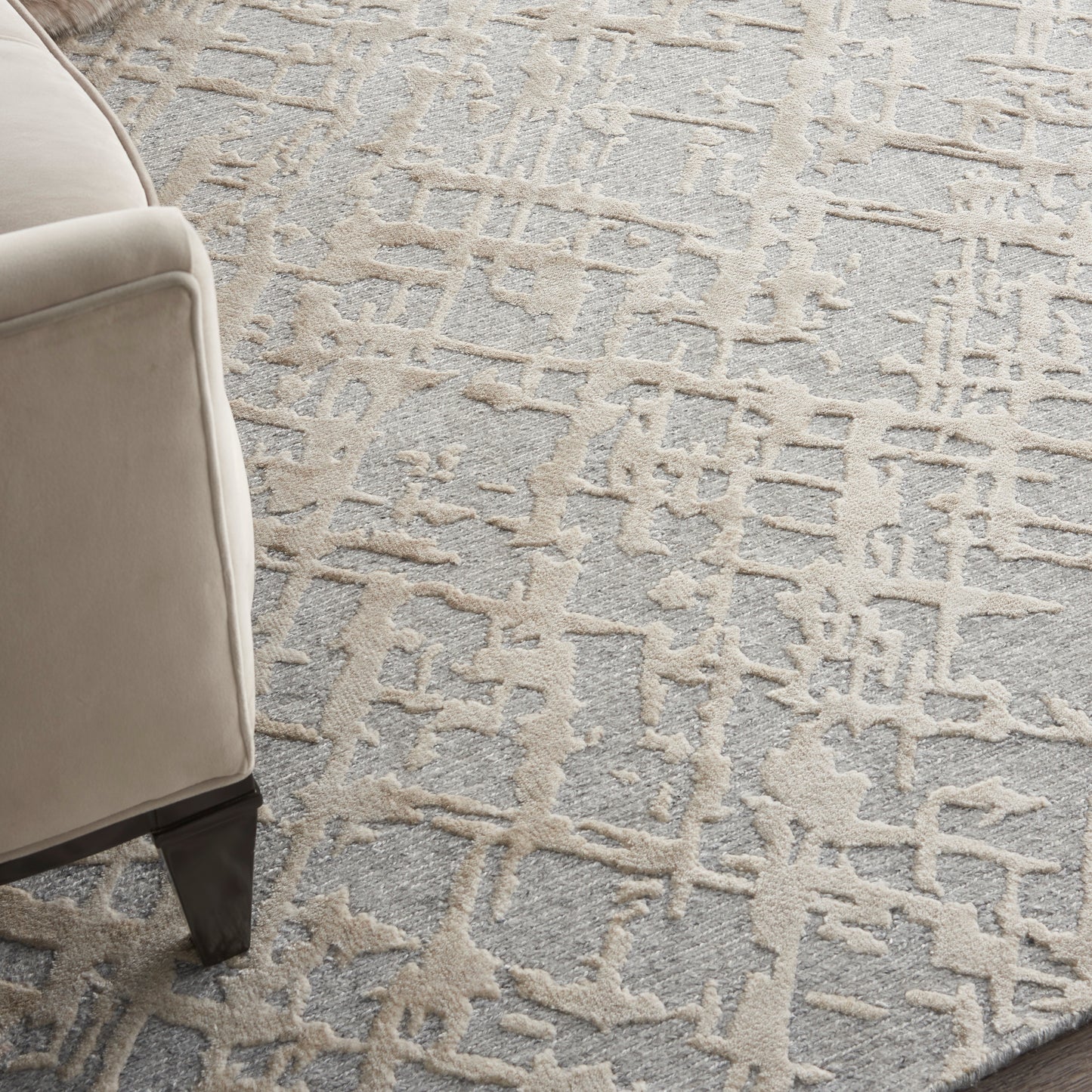 Gray area rug with beige abstract raised pattern; partial beige sofa leg visible on left.