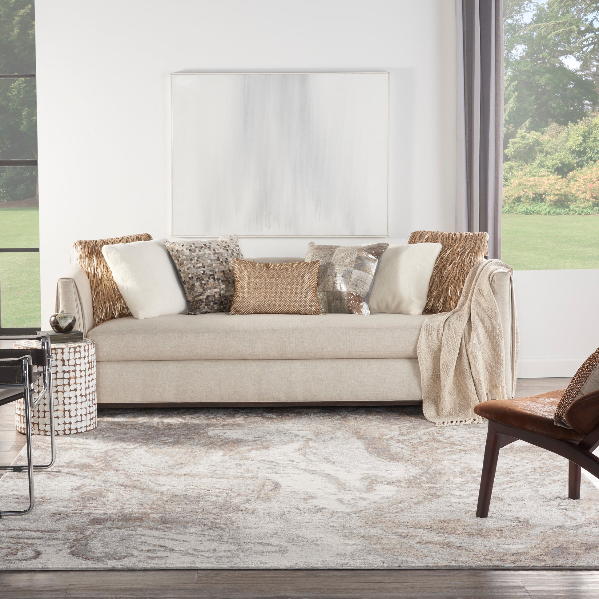 Beige sofa with diverse textured pillows, draped throw, woven side table, gray abstract rug in bright living room