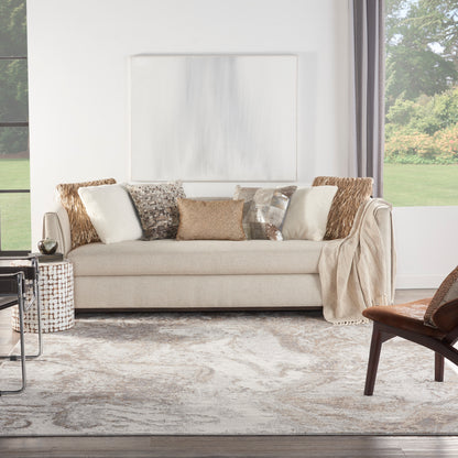 Beige sofa with diverse textured pillows, draped throw, woven side table, gray abstract rug in bright living room