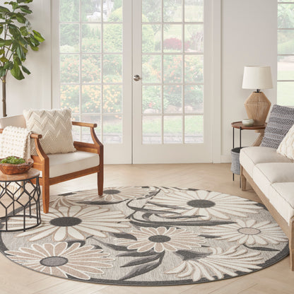 Round floral rug in beige and gray under a light living room with wood armchairs, neutral sofa, plant, and French doors.