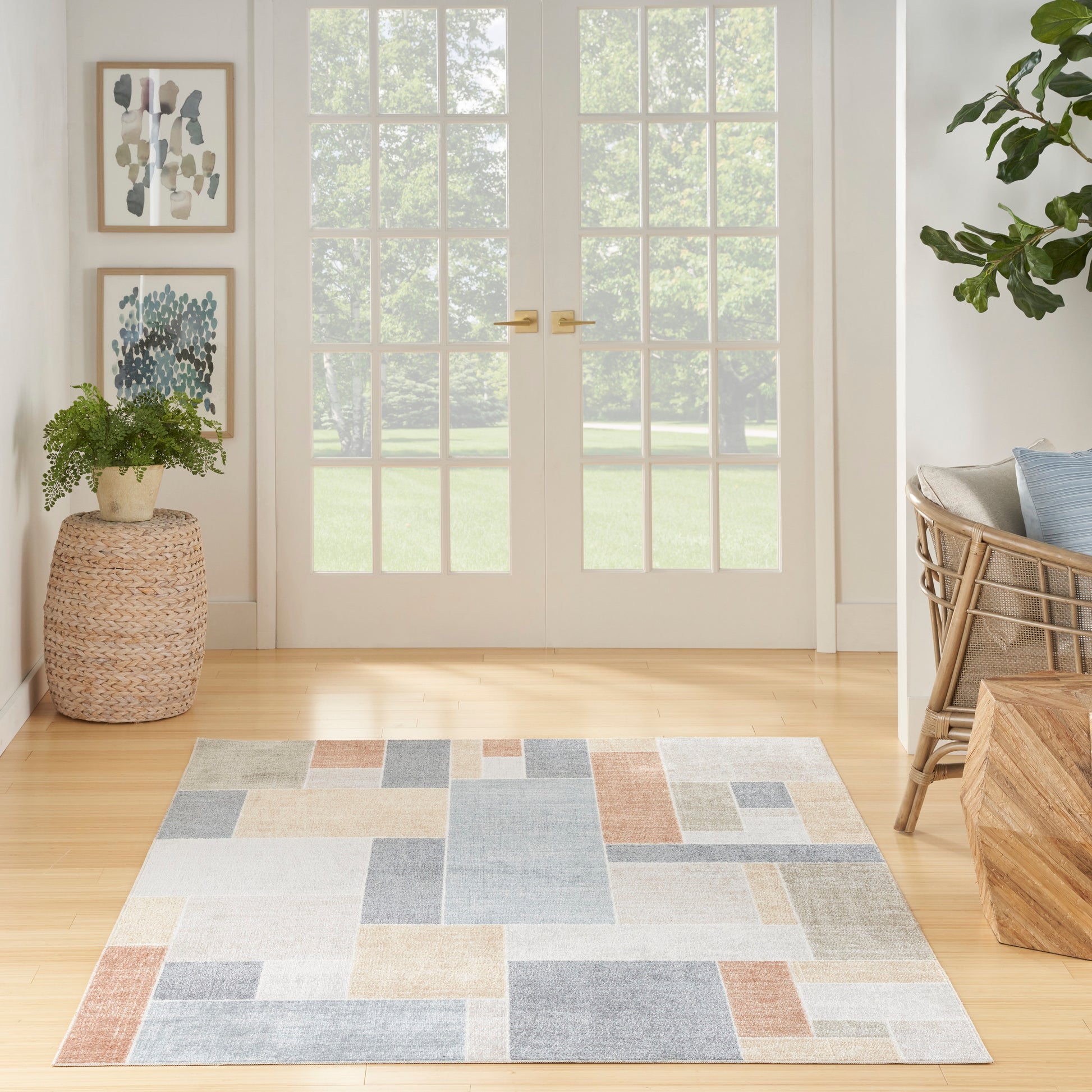Geometric pastel rug on light hardwood floors in bright coastal entryway with potted plant, framed art, and rattan chair.