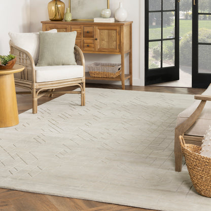 Neutral living room with wicker armchair, light beige geometric rug, wooden console table, wicker basket & French doors.