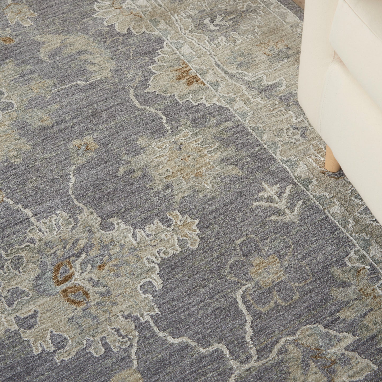 Blue-gray area rug with beige floral medallion pattern; traditional damask style near a white sofa.