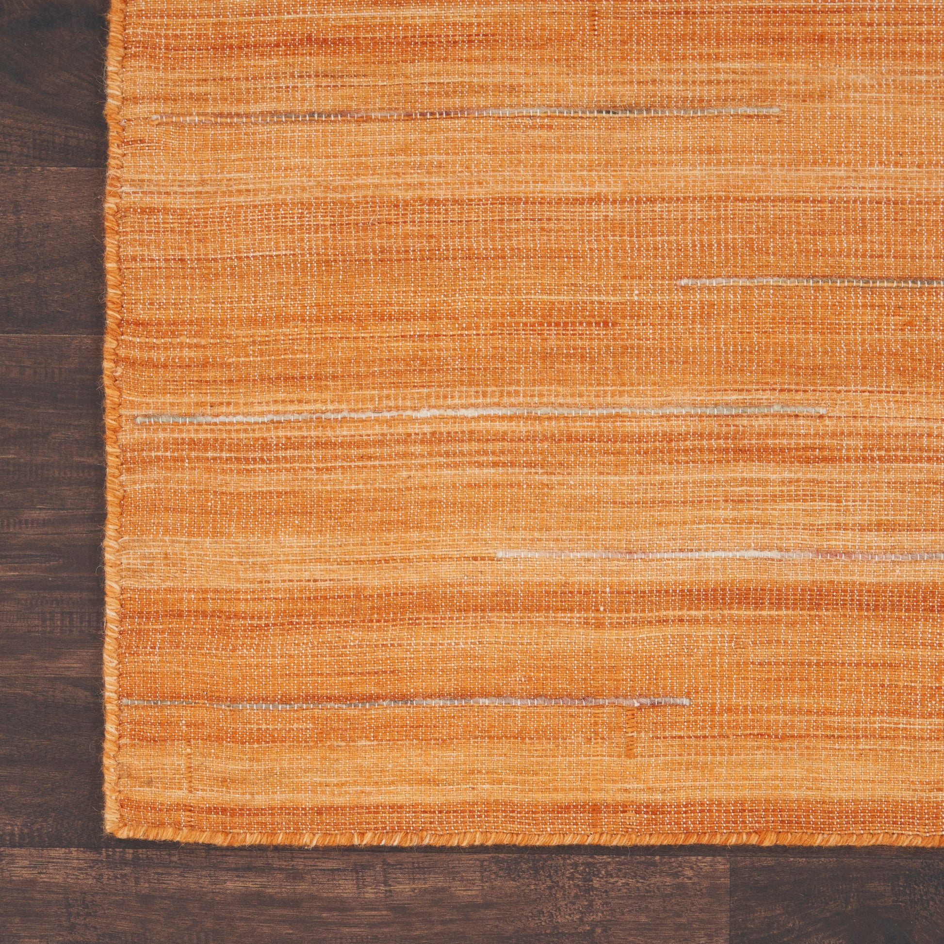 Orange woven rug with subtle white streaks and a small fringe edge on dark wood floor.