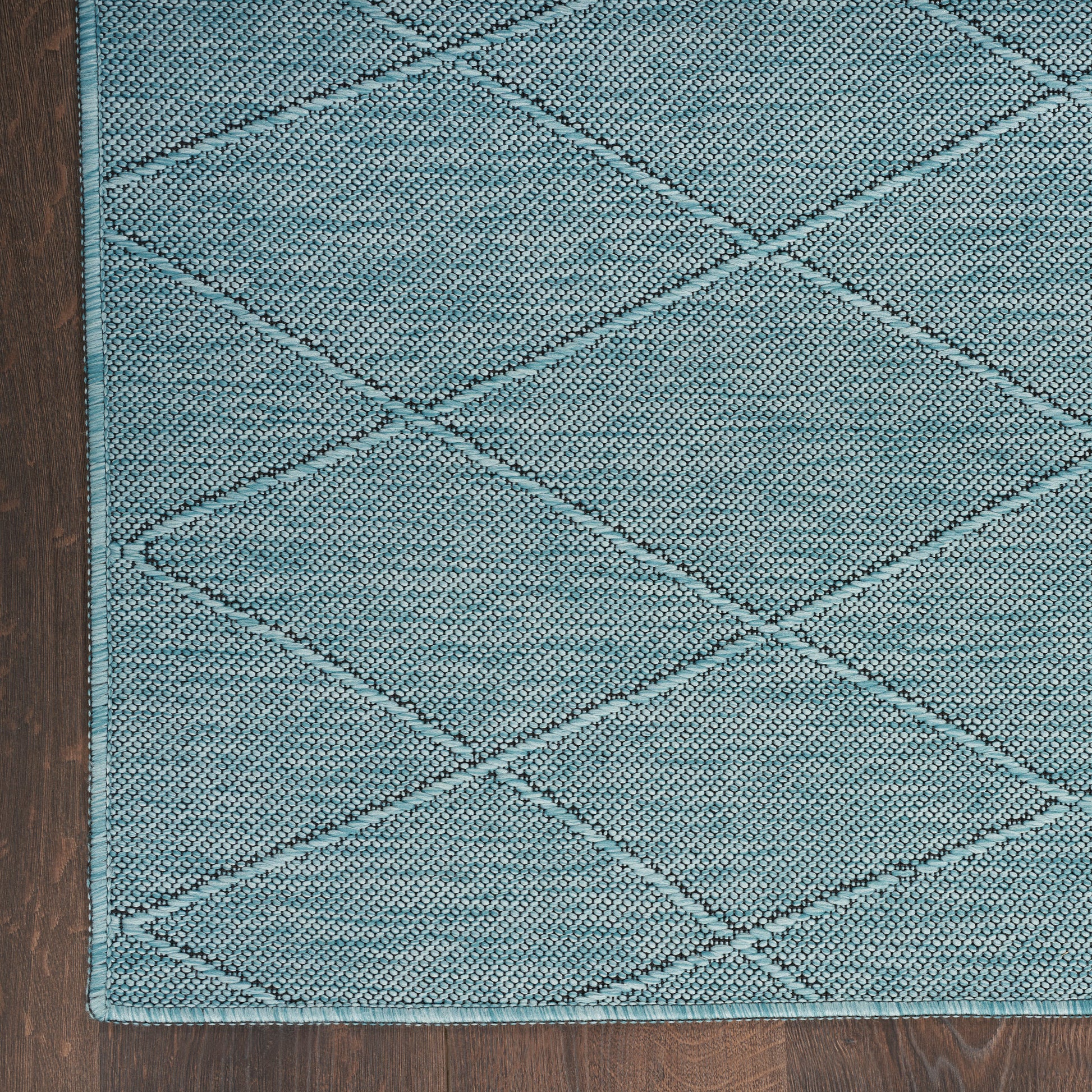 Teal diamond-quilted rug with textured weave and stitched border on wooden floor.