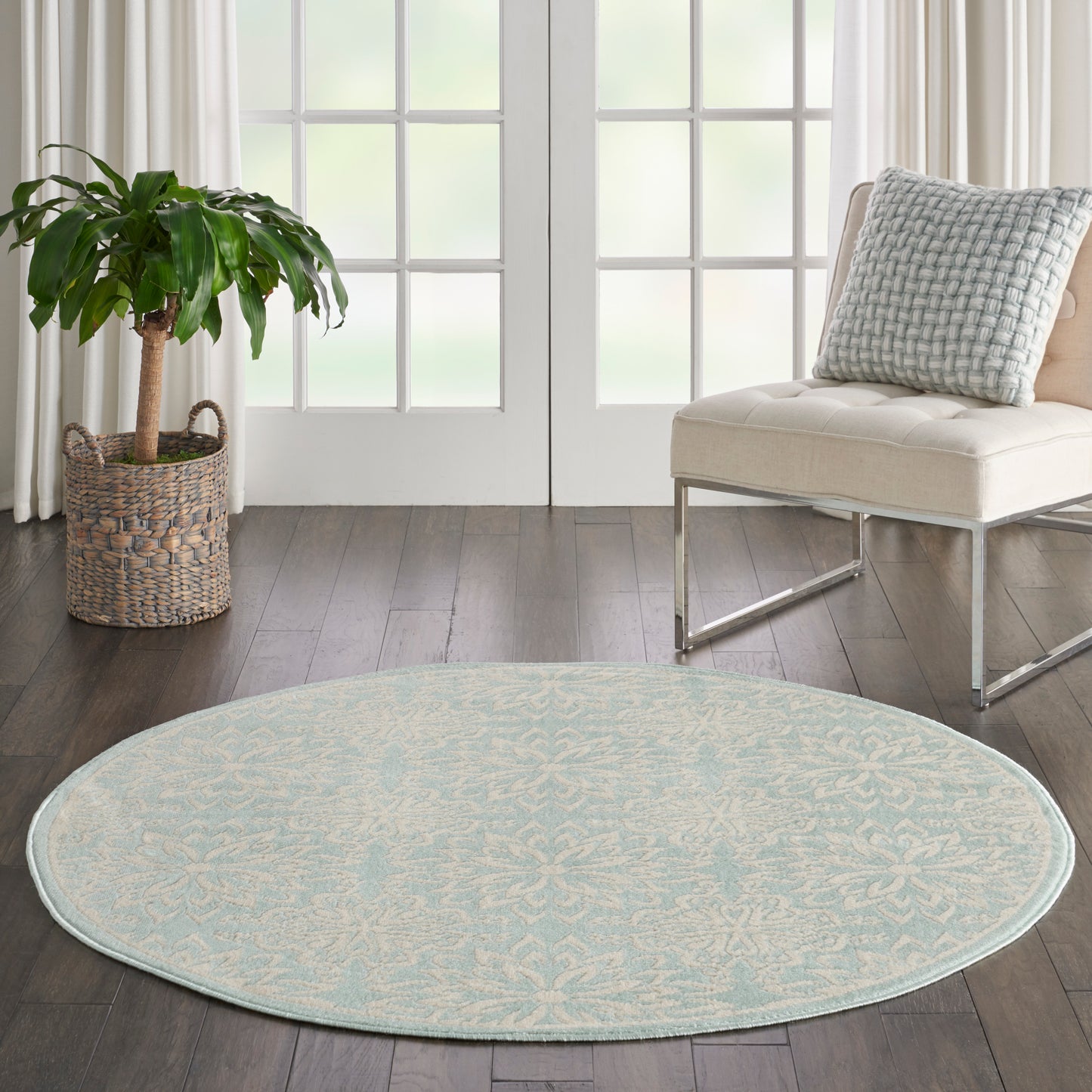 Round pale blue patterned area rug in a bright living room with a potted plant, woven basket, and cream lounge chair.