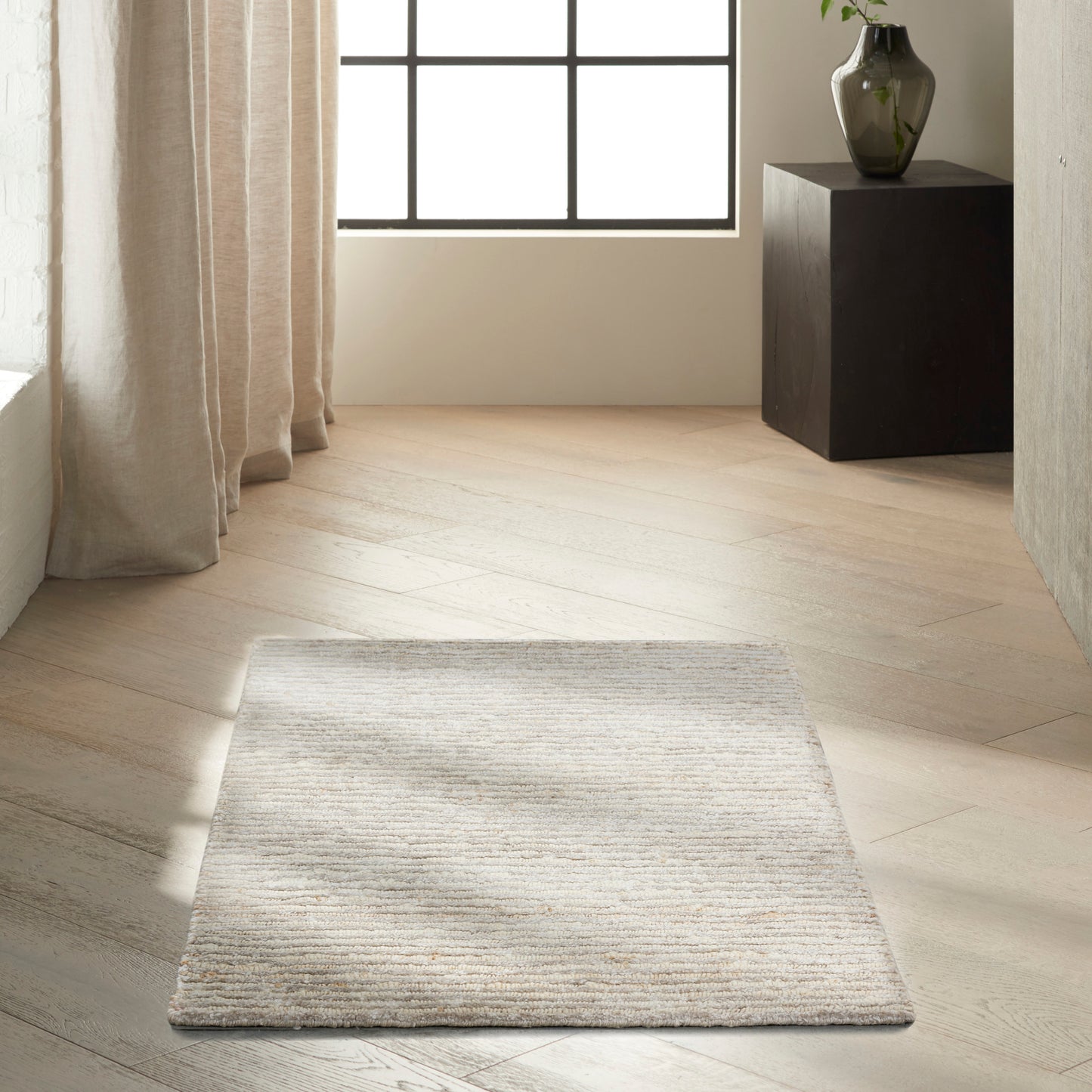 Rectangular beige & gray striped textured rug on light wood floor in a bright minimalist room.