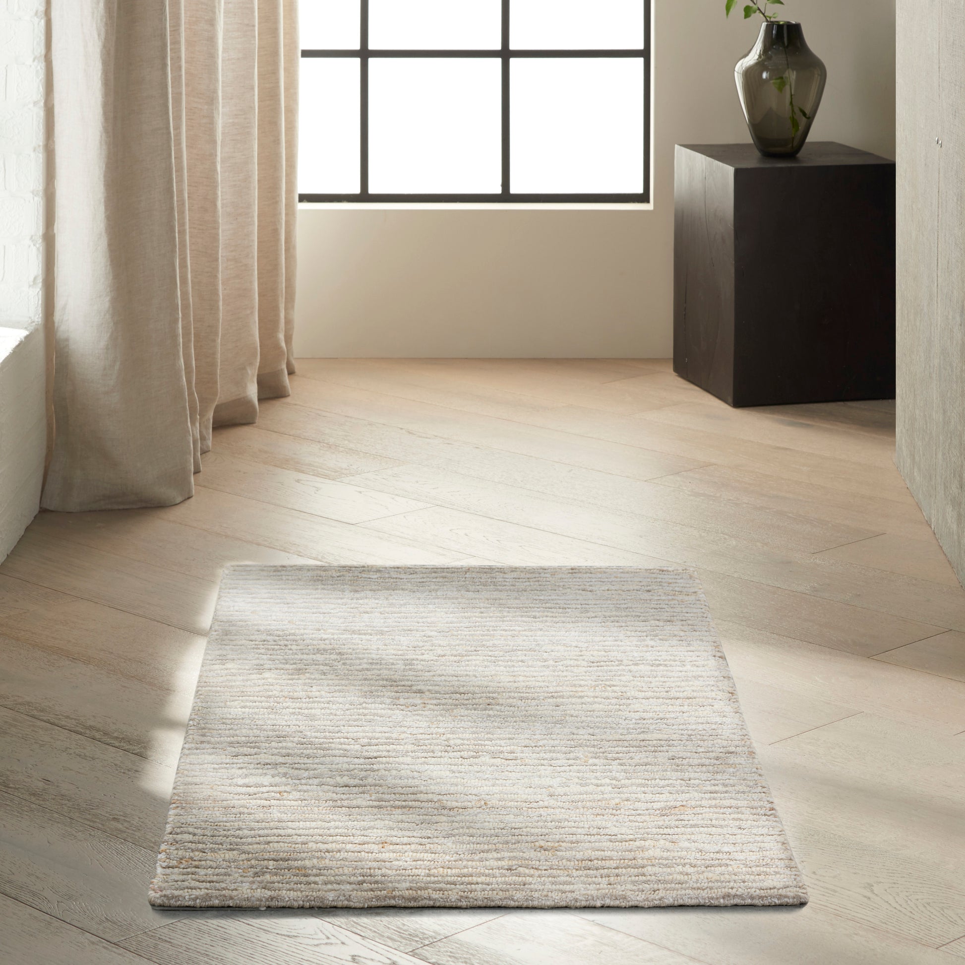 Rectangular beige & gray striped textured rug on light wood floor in a bright minimalist room.
