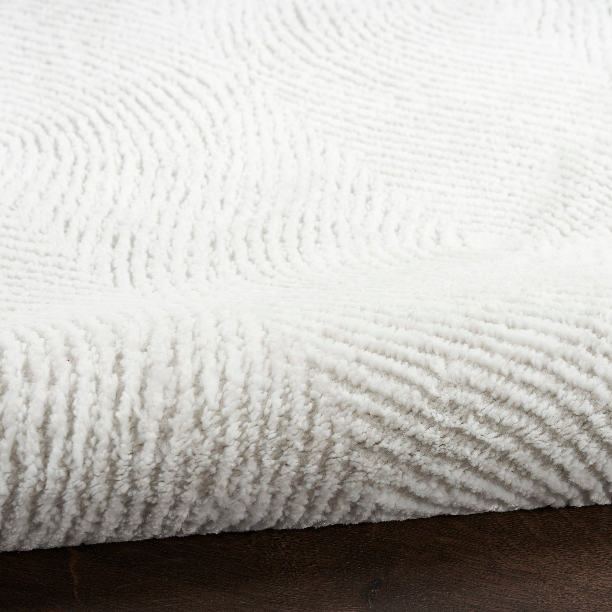 White fluffy textured rug with raised loop pile draped over dark wooden surface.