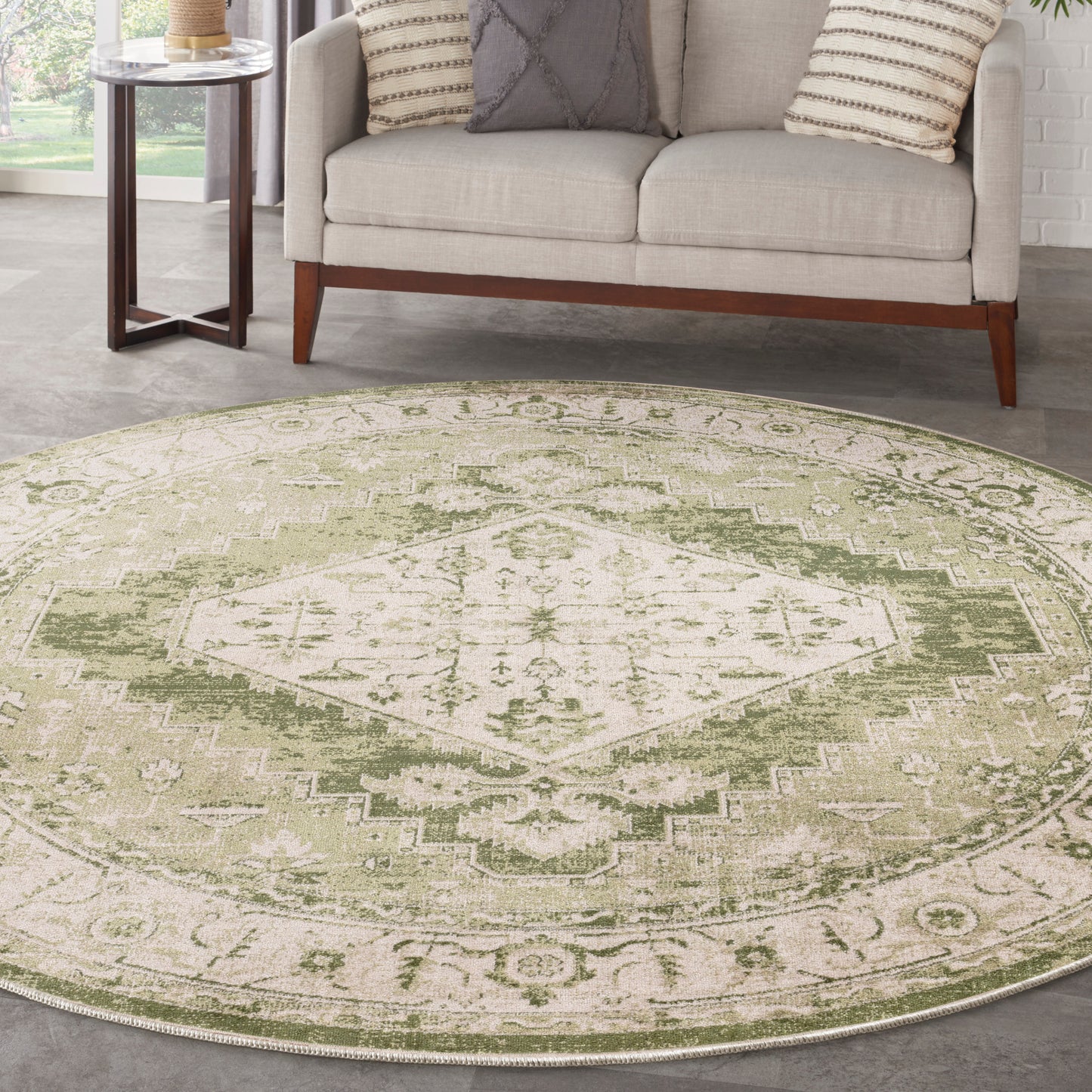 Round sage green and cream distressed rug with a geometric medallion in a living room with a beige sofa.