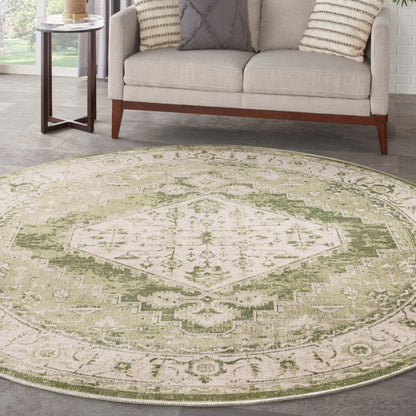 Round sage green and cream distressed rug with a geometric medallion in a living room with a beige sofa.