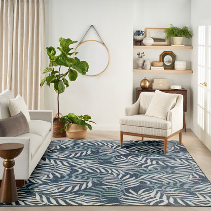 Cozy living room: blue fern-leaf patterned rug, cream sofa, striped armchair, wooden legs, potted plants, round wall hoop.