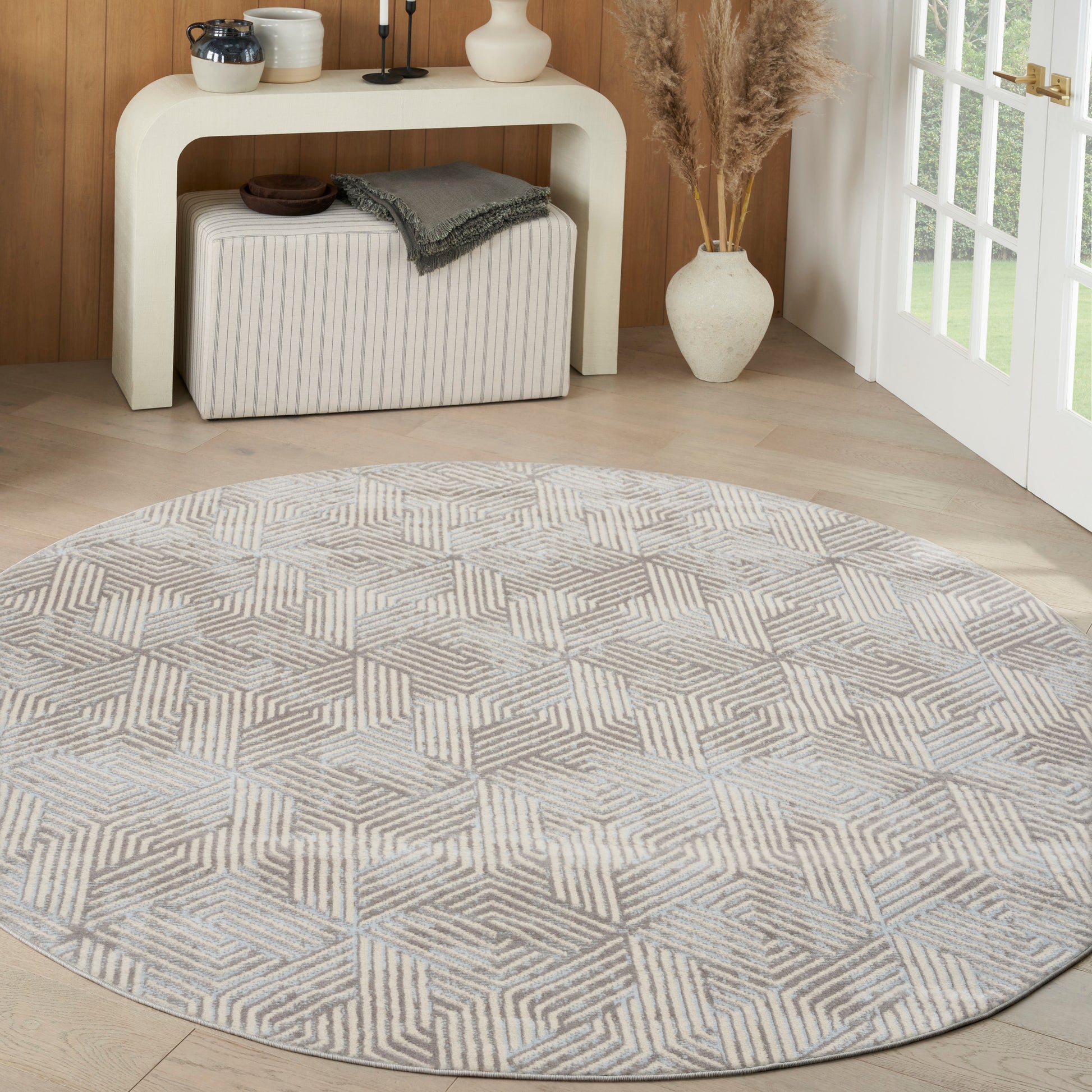 Round light gray geometric patterned rug on pale wood floor with a modern cream console & decorative items.