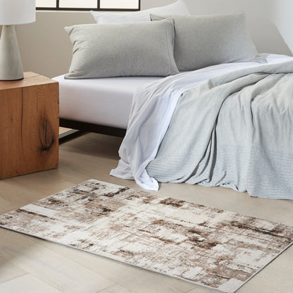 Cozy modern bedroom with light gray bedding and pillows, white sheets, a beige-brown rug, and a wooden bedside table.