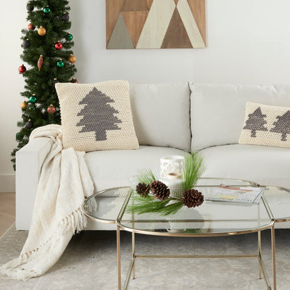Cozy living room with a Christmas tree, beige sofa, treepattern knitted cushions, and glass coffee table with pine cones.