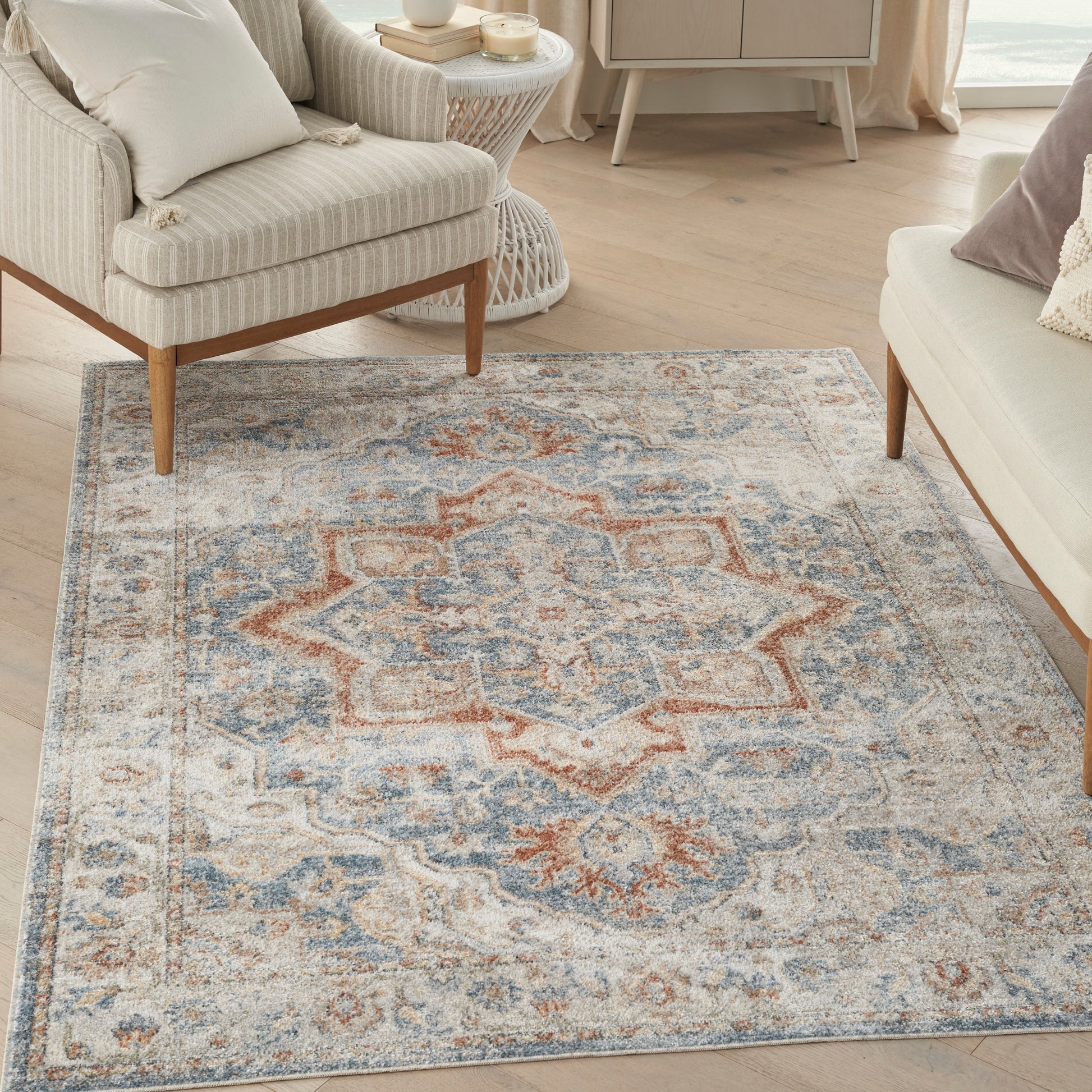 Blue, beige and rust oriental rug with central medallion, in a light living room with beige-striped chairs and wooden legs.