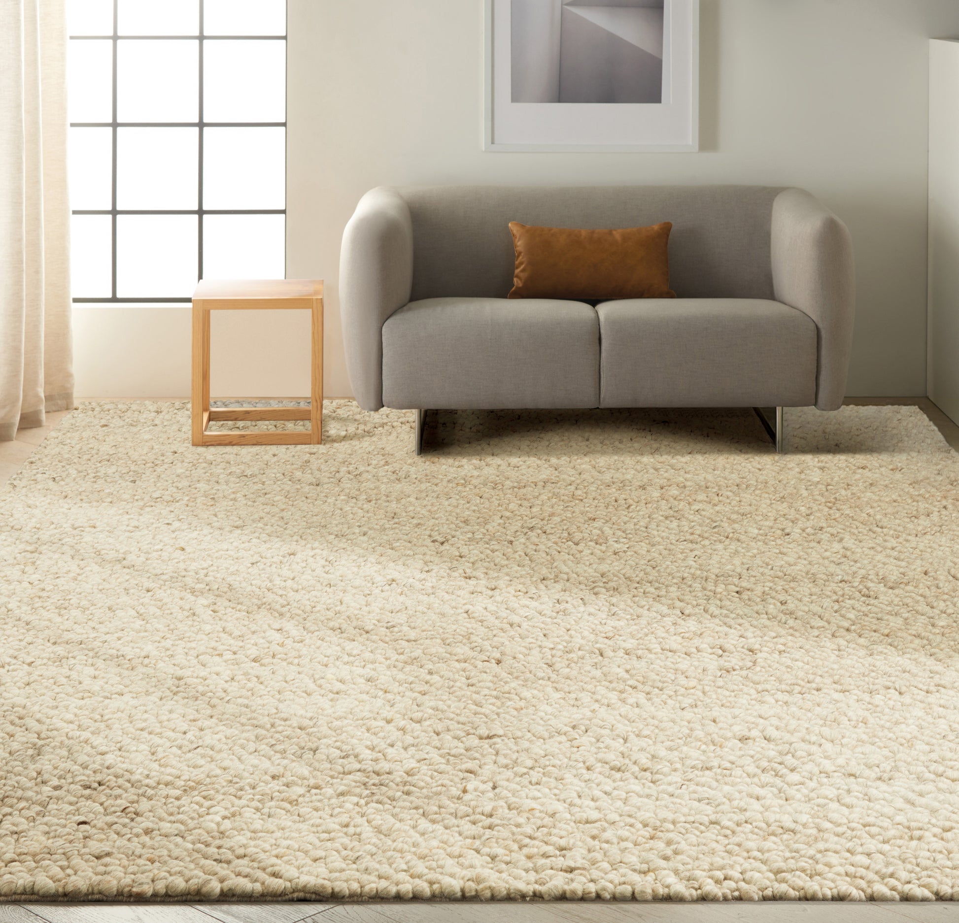 Cream shag rug with a gray fabric loveseat and tan pillow on it, in a minimalist living room with a light wood cube side table.