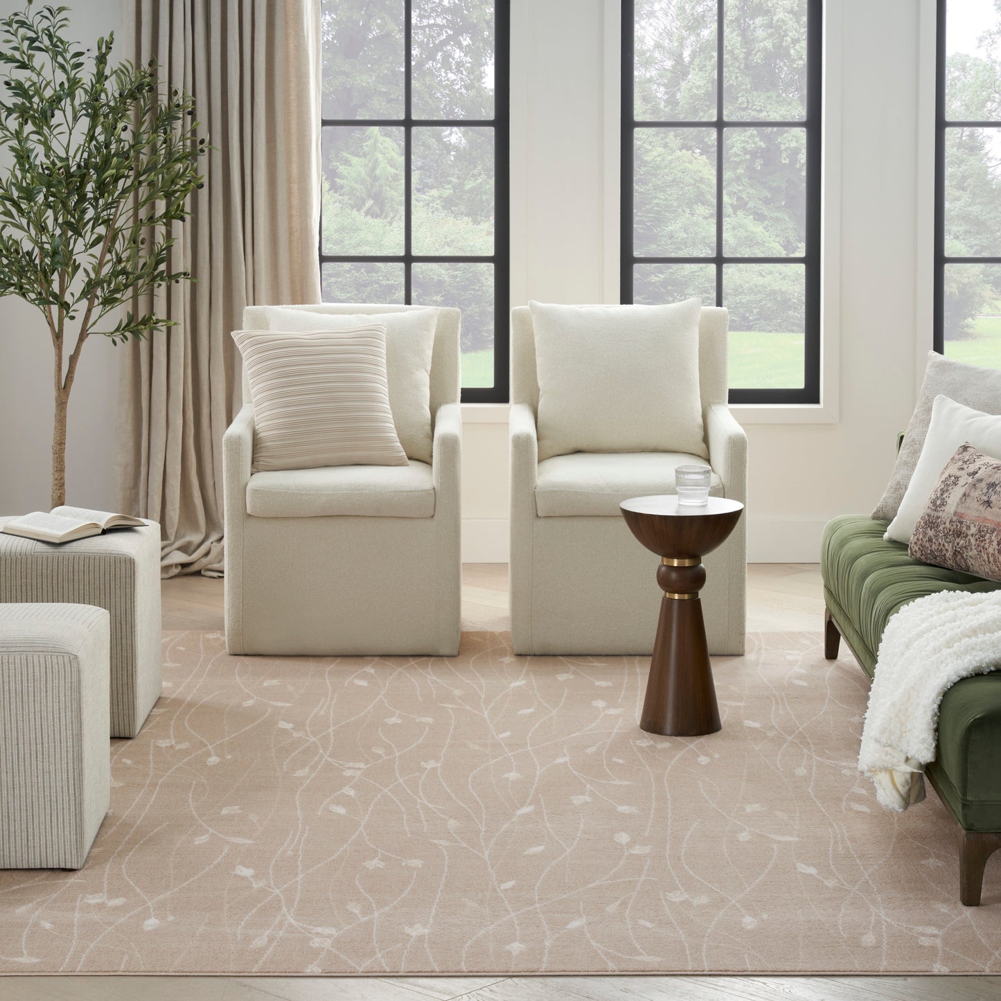Neutral living room with two beige armchairs, green sofa, beige rug, wooden side table, potted plant & black windows.