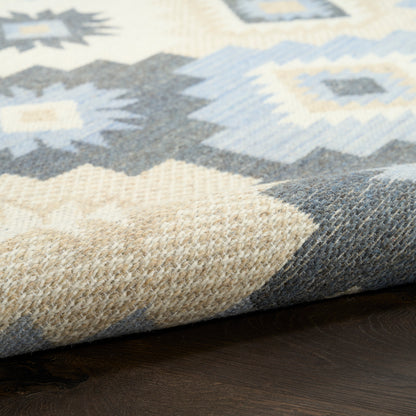 Close-up of a woven geometric area rug with blue, beige and gray diamond patterns on a dark wooden floor.