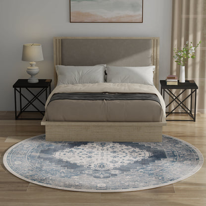 Beige upholstered platform bed with gray headboard, blue patterned rug, two black metal nightstands, lamp, plant.