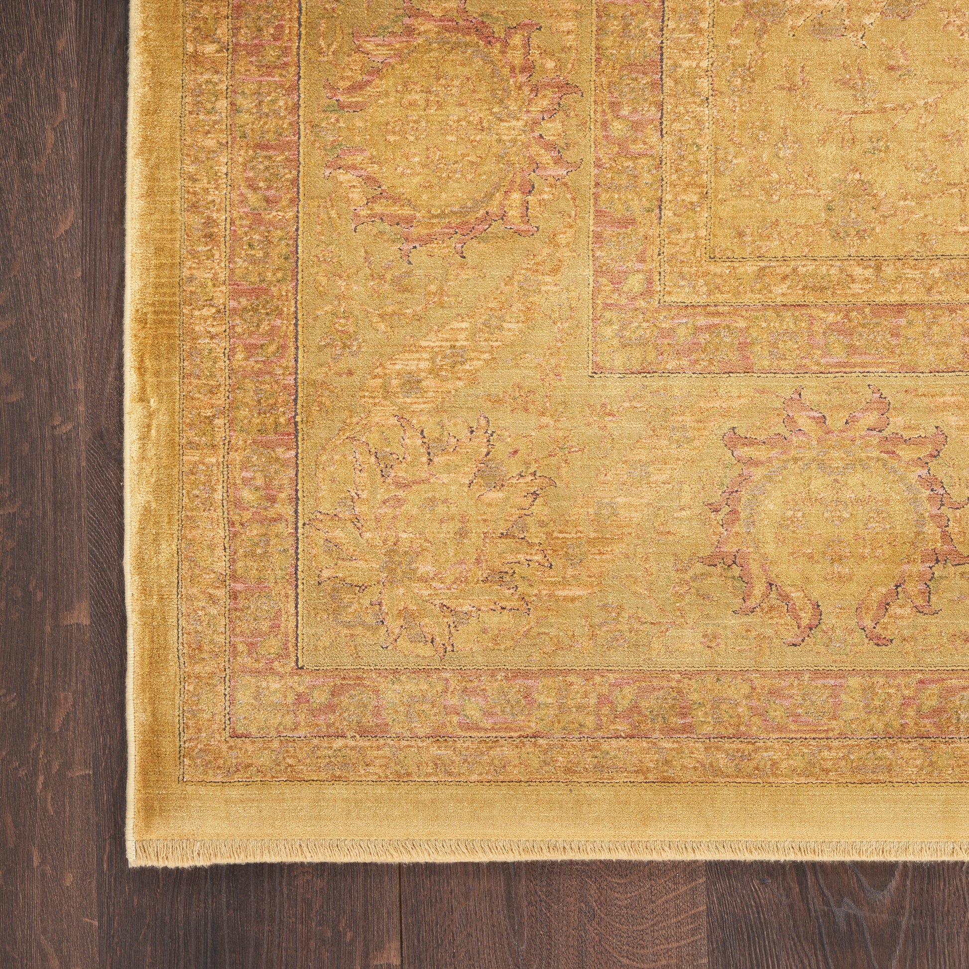 Golden yellow Oriental rug with pink floral motif and fringed edges on dark wood floor.