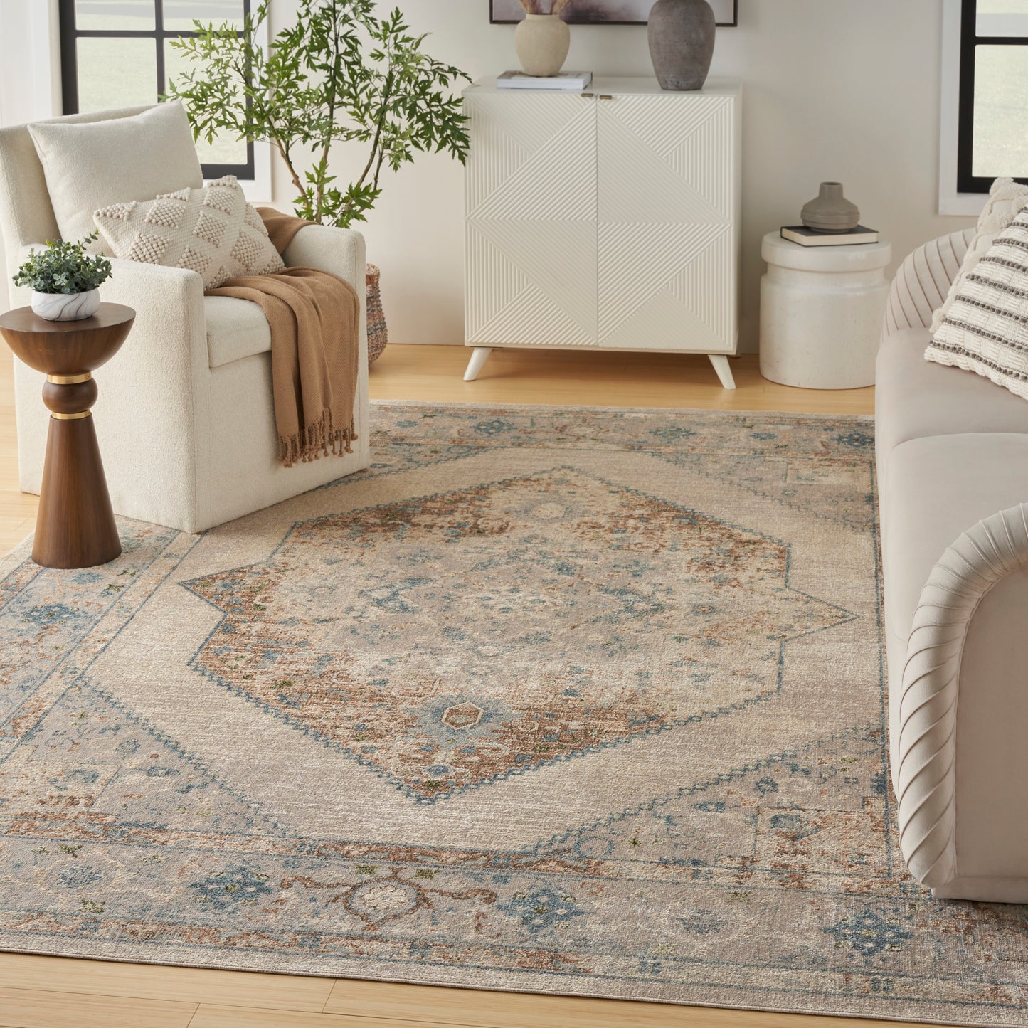 Neutral living room with a large beige-blue oriental-inspired rug, cream sofa, white cabinet, plants, and soft throws.
