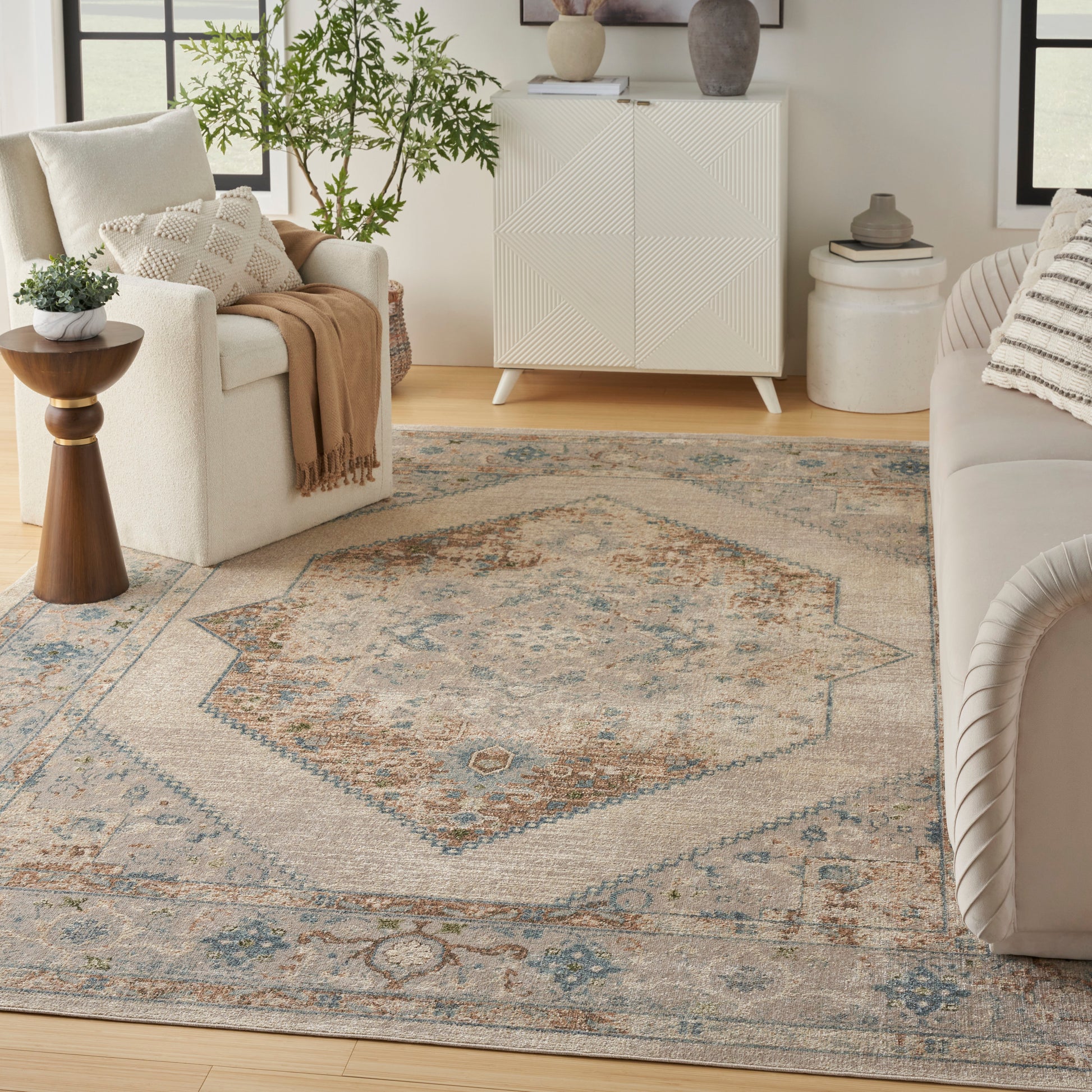Neutral living room with a large beige-blue oriental-inspired rug, cream sofa, white cabinet, plants, and soft throws.