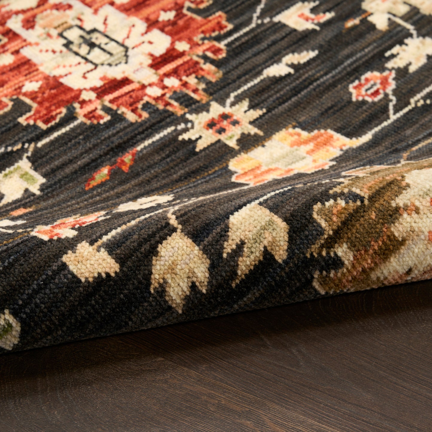 Persian-inspired rug with dark navy base, red, cream & green floral motifs; folded edge on a wooden floor.