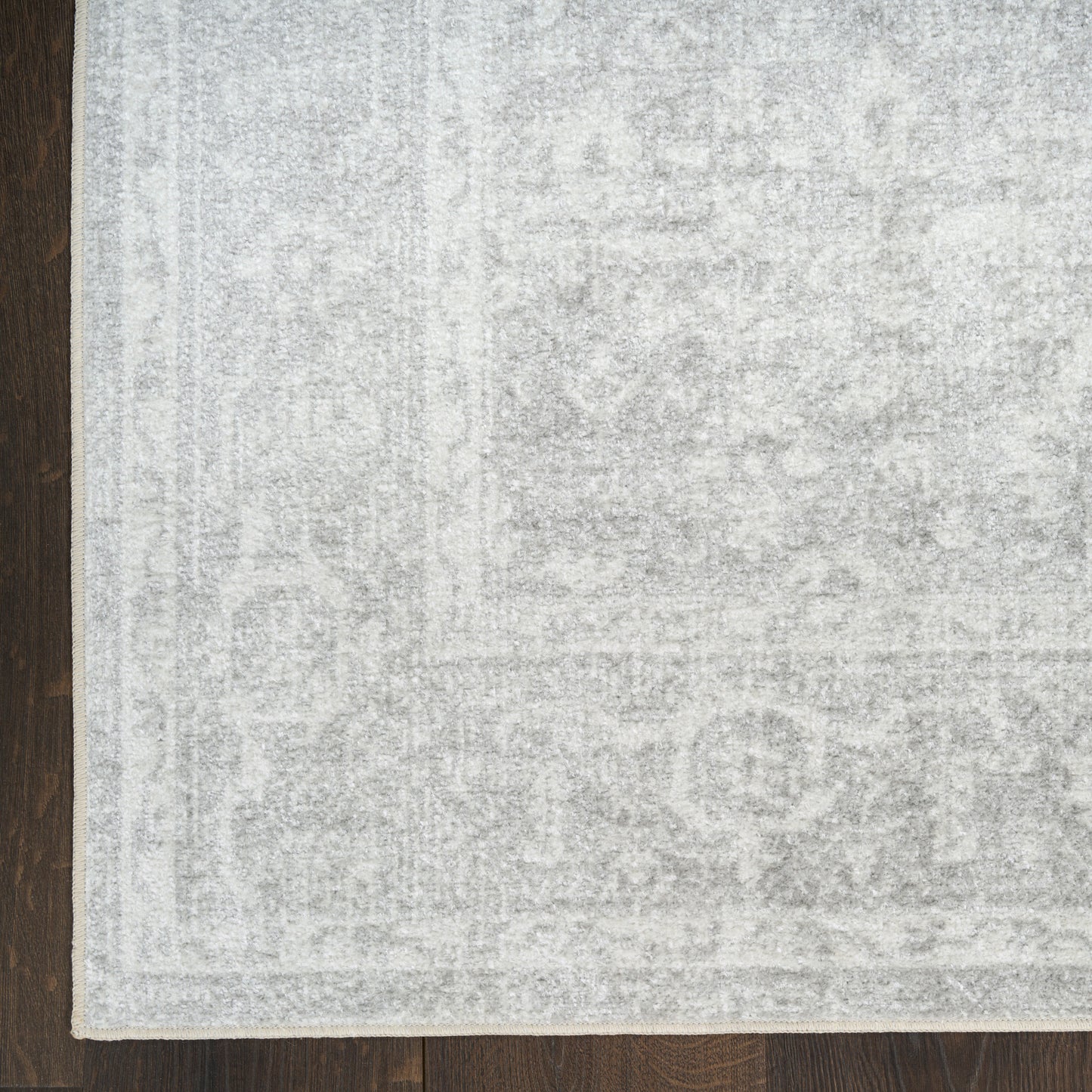 Light gray distressed area rug with subtle oriental pattern on dark wood floor; pale border visible.