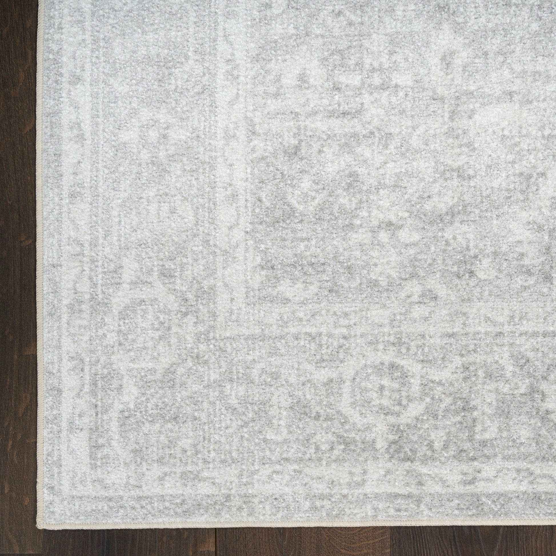 Light gray distressed area rug with subtle oriental pattern on dark wood floor; pale border visible.