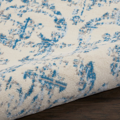 Blue and ivory patterned area rug with a distressed botanical motif, soft woven texture on dark wooden floor.