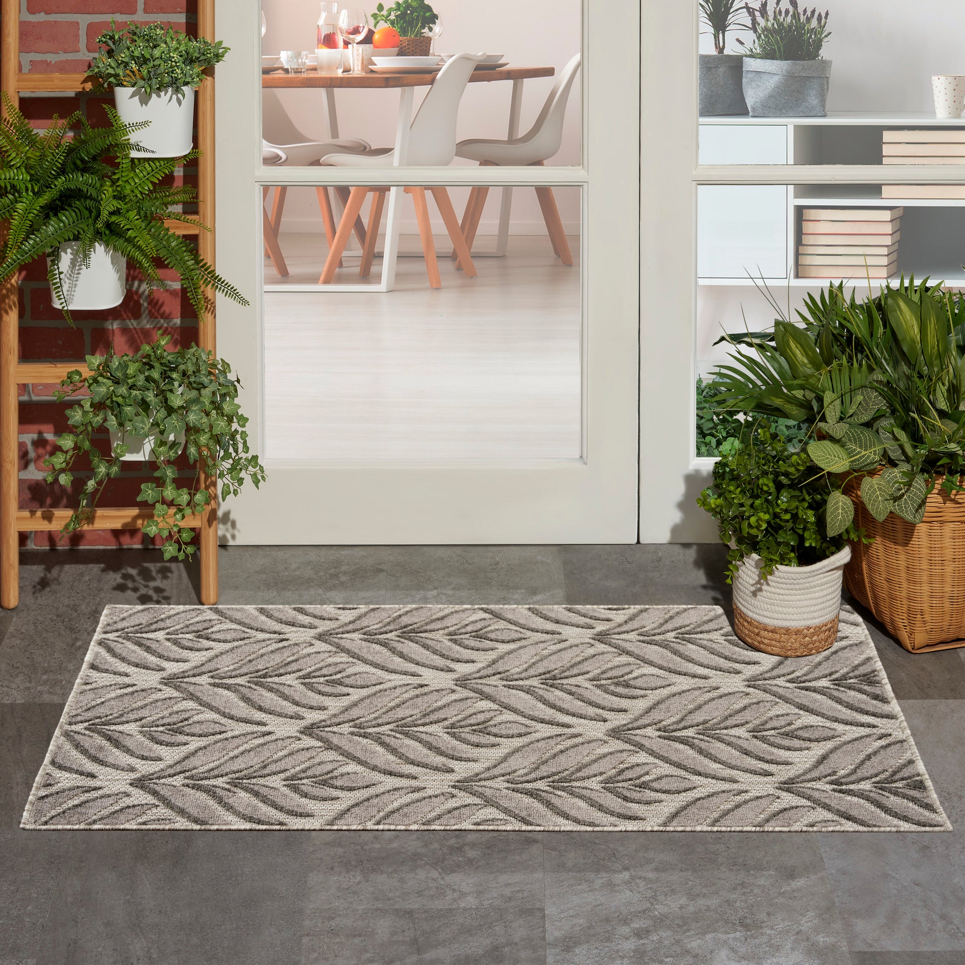 Gray leaf rug on dark tile, plants in baskets beside glass doors opening to a bright dining room.