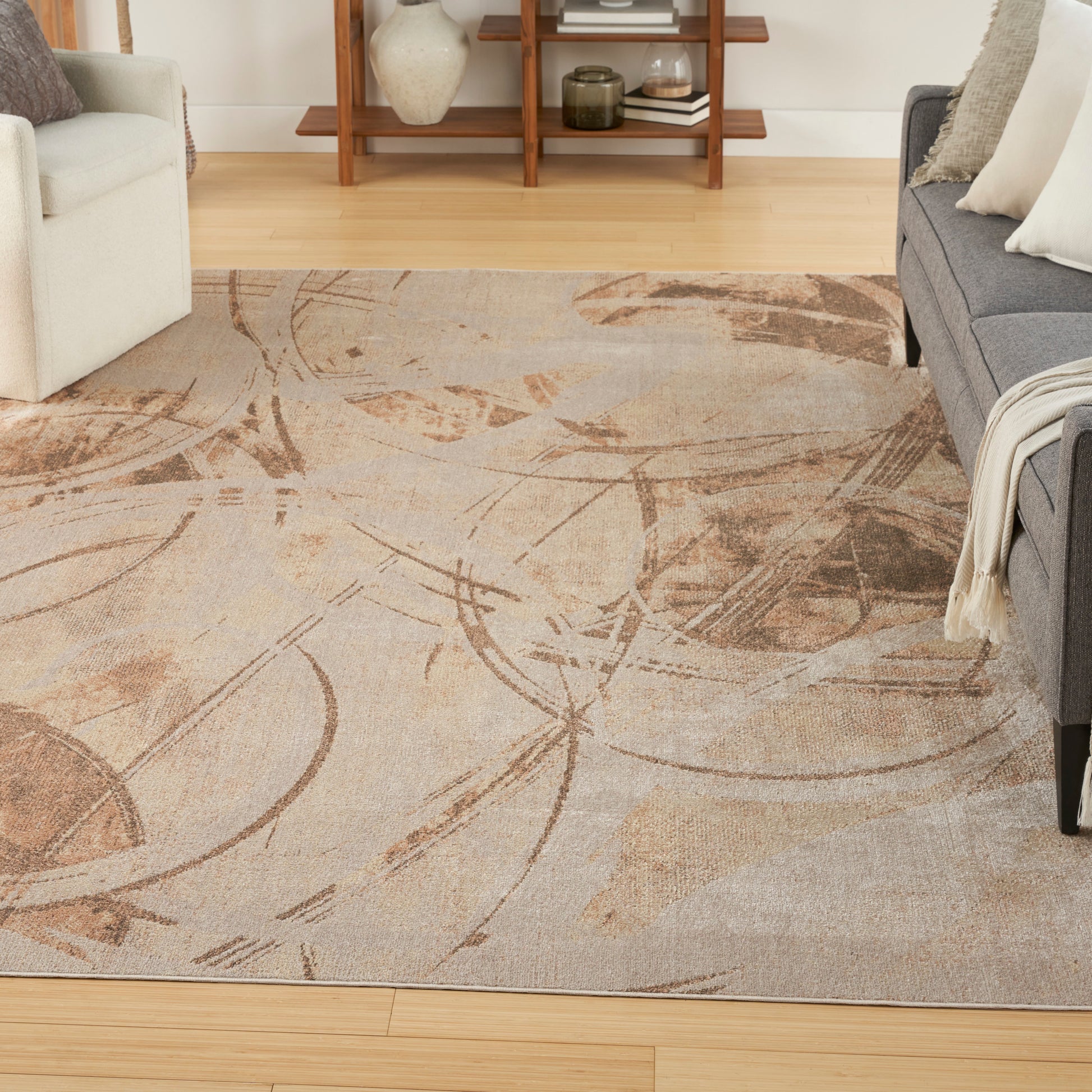 Abstract beige and brown patterned area rug in a living room with cream and gray sofas.