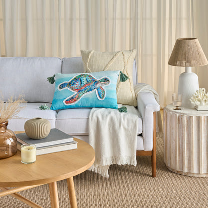 Rectangular decorative throw pillow on a light gray fabric sofa in a coastal living room, multicolor coastal pattern.