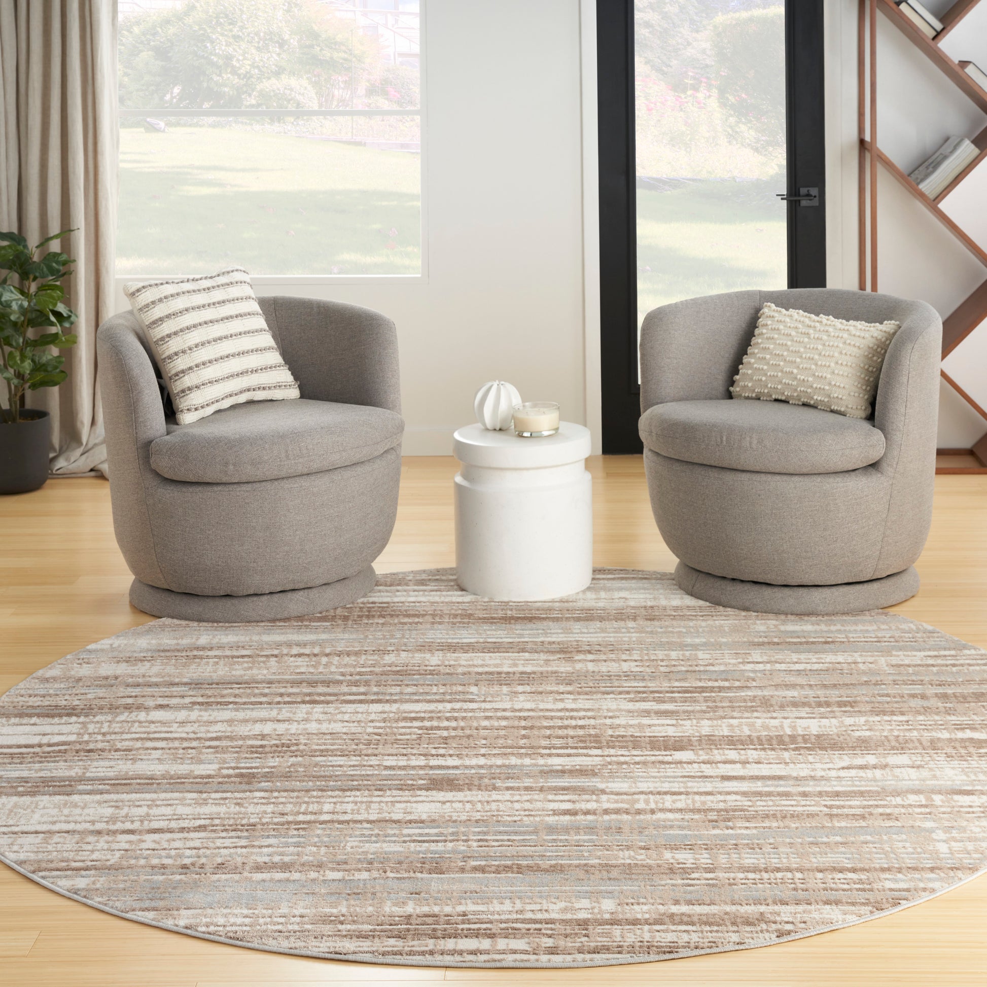 Two gray round lounge chairs with striped and textured cushions flank a white circular side table on a beige round rug.