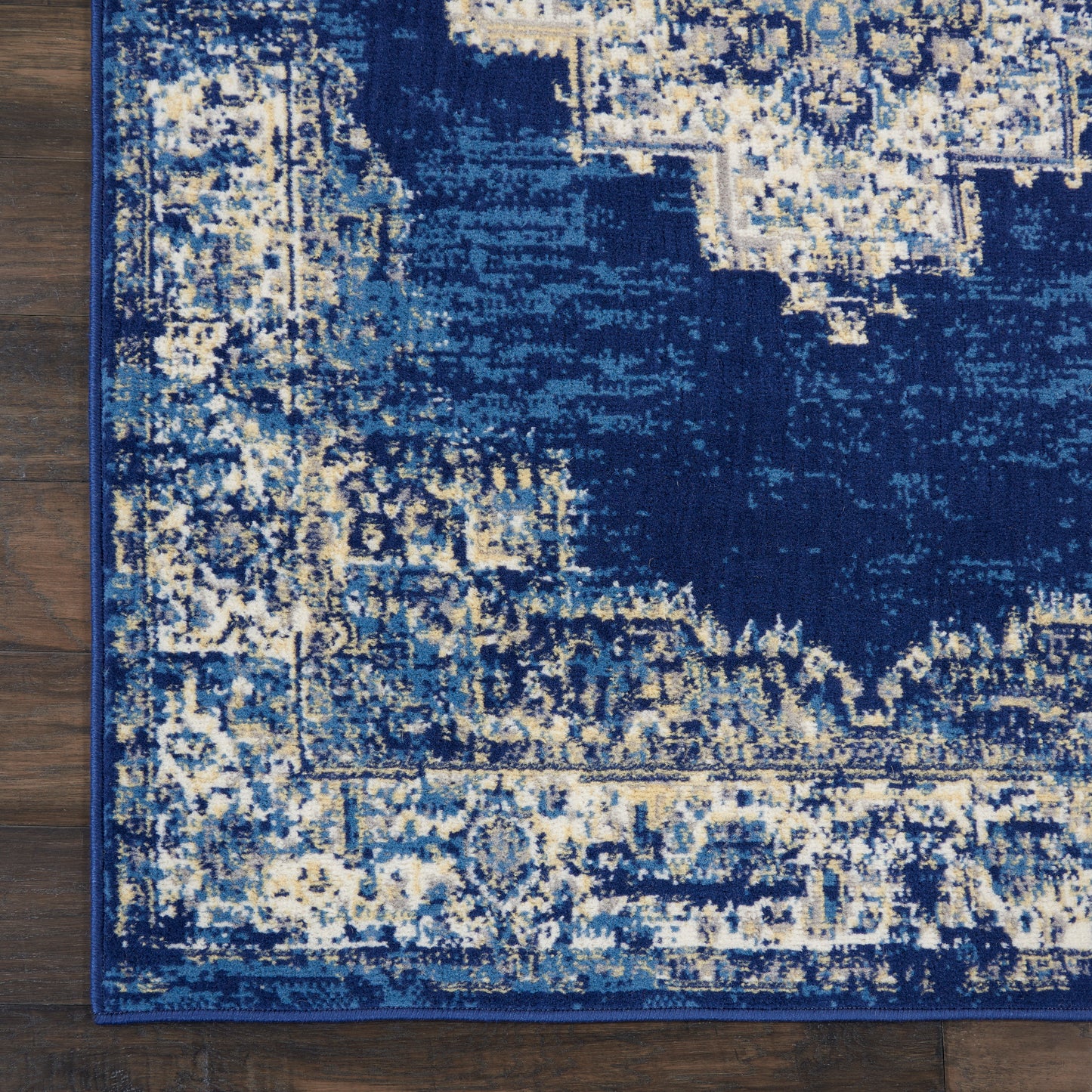 Blue distressed area rug with cream geometric pattern and dark border on wooden floor.