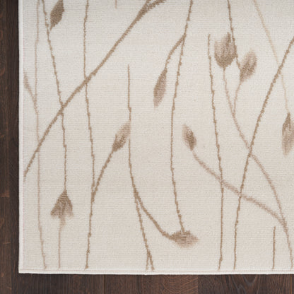 Beige rectangular area rug with subtle brown branch motif, white border, on dark hardwood floor.