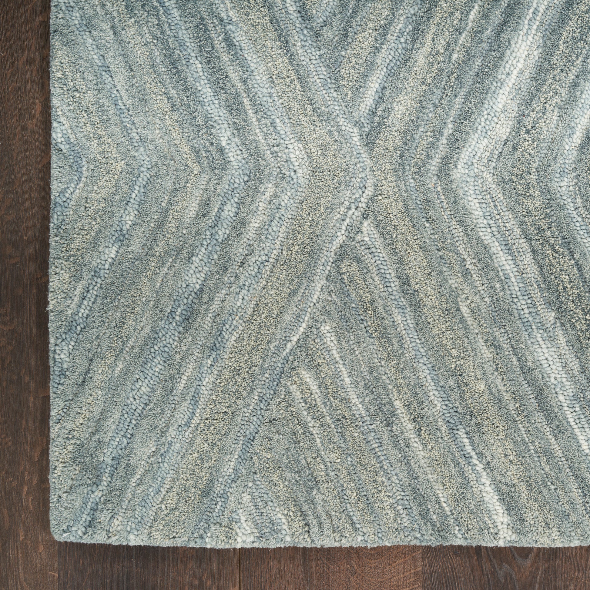 Rectangular blue-gray geometric rug with a textured wavy chevron pattern and tufted pile on a dark wood floor.