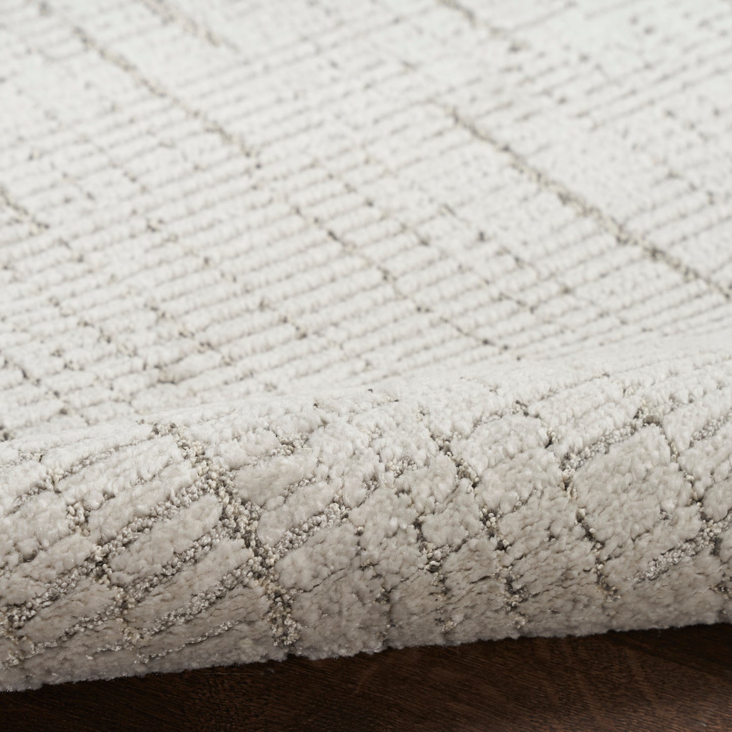 Cream textured rug with a subtle diamond lattice pattern; low-pile cut-loop rug on dark wood floor.