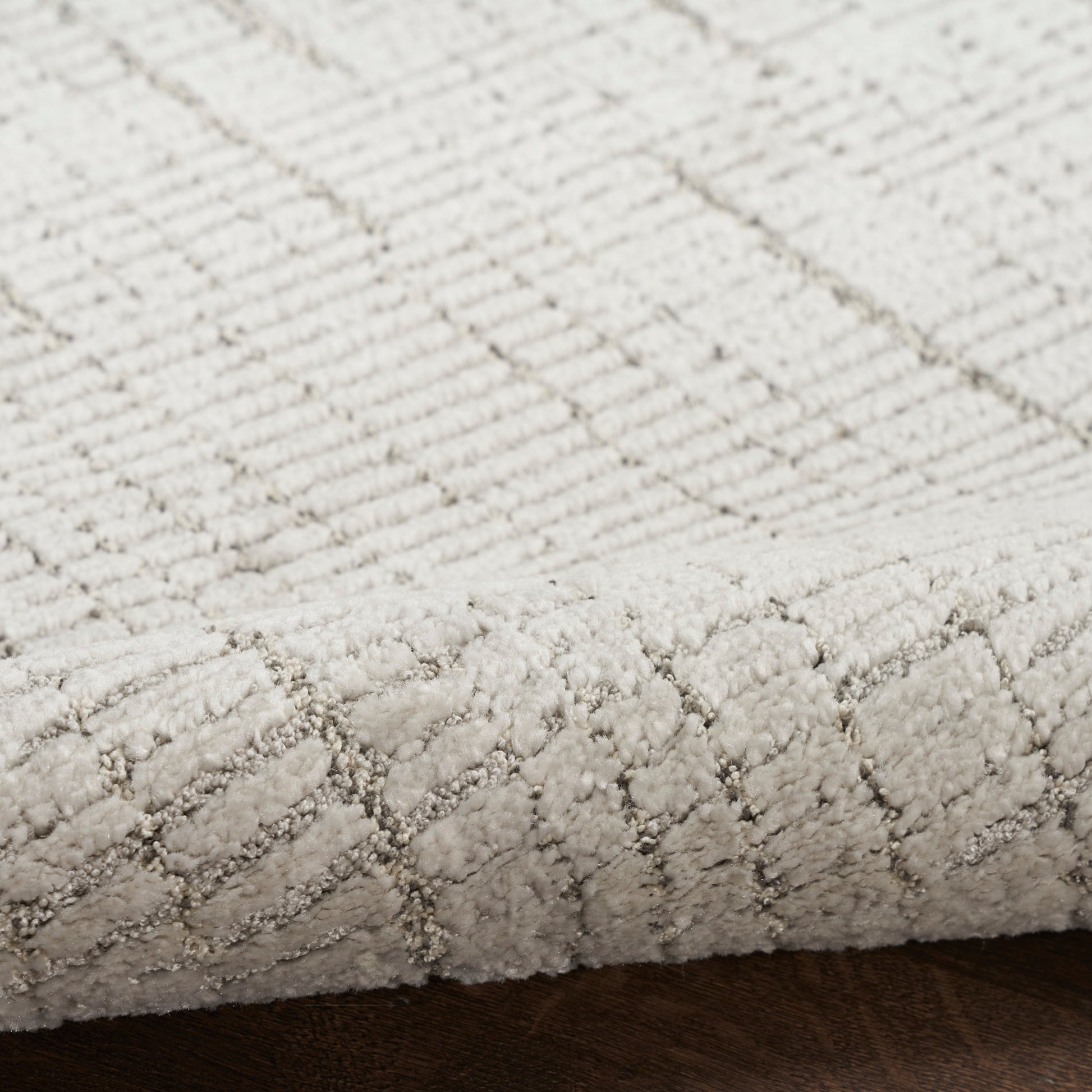 Cream textured rug with a subtle diamond lattice pattern; low-pile cut-loop rug on dark wood floor.