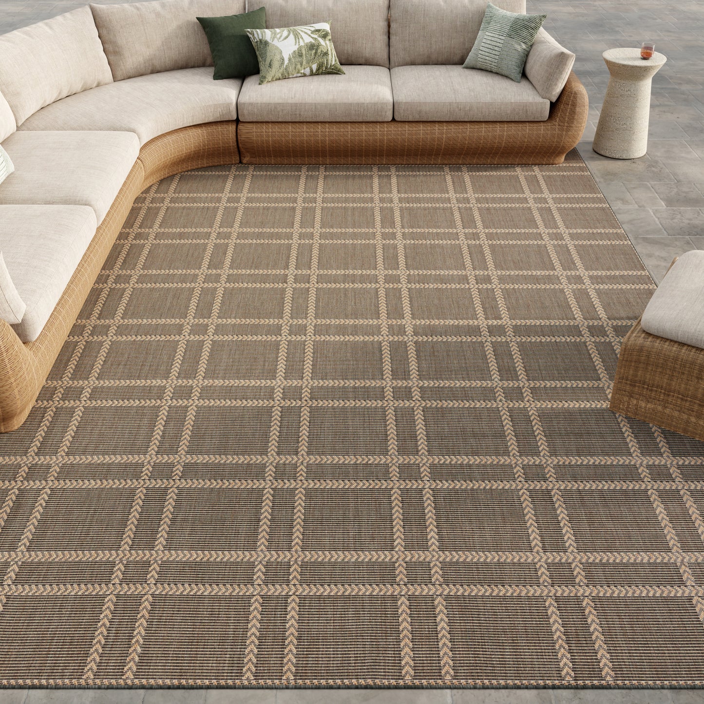Curved tan wicker sectional with beige cushions on a brown plaid woven rug; coastal neutral living room.