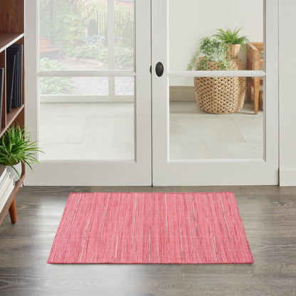 Soft pink rectangular rug on dark wood floor in front of glass doors; greenery and wicker basket in background.