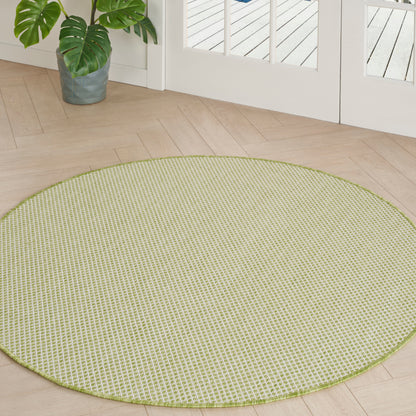 Round lime-green woven rug on light wood floor by glass doors; potted monstera plant nearby.