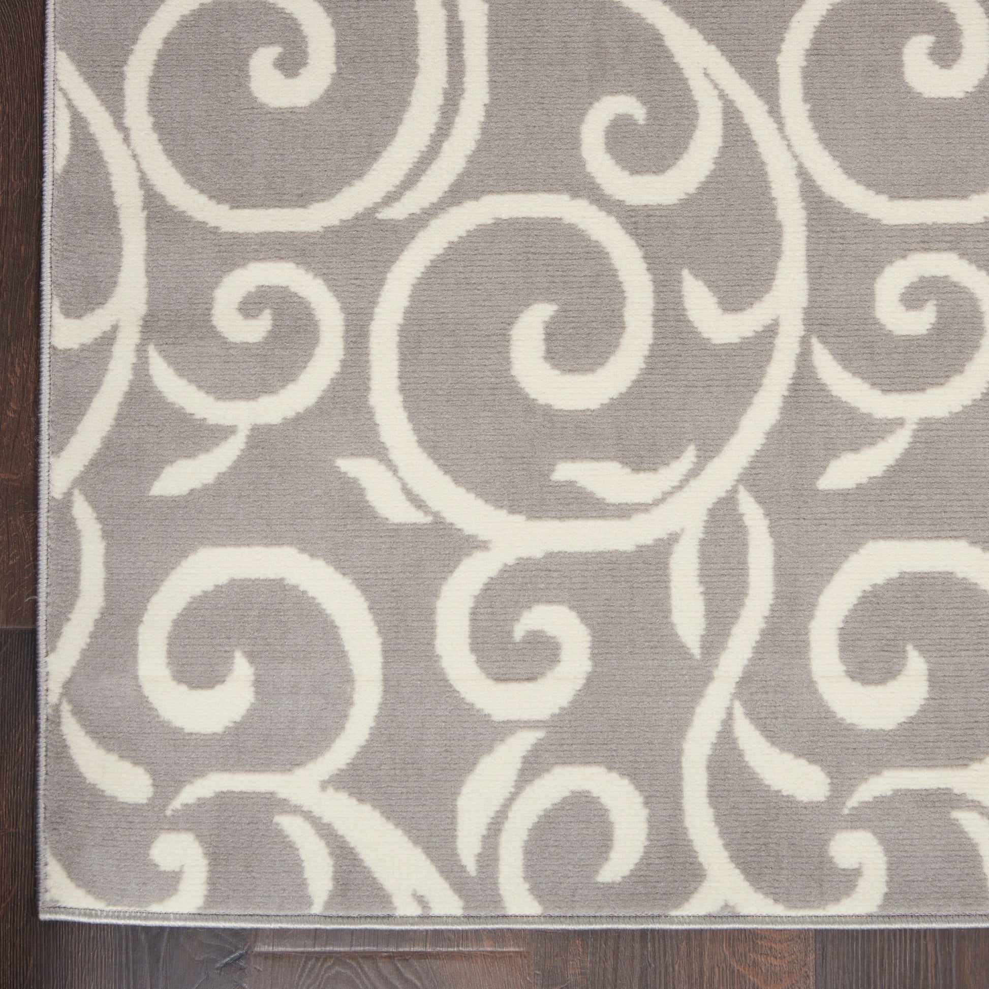 Gray rug with white swirling scroll pattern and thin border on dark wood floor.