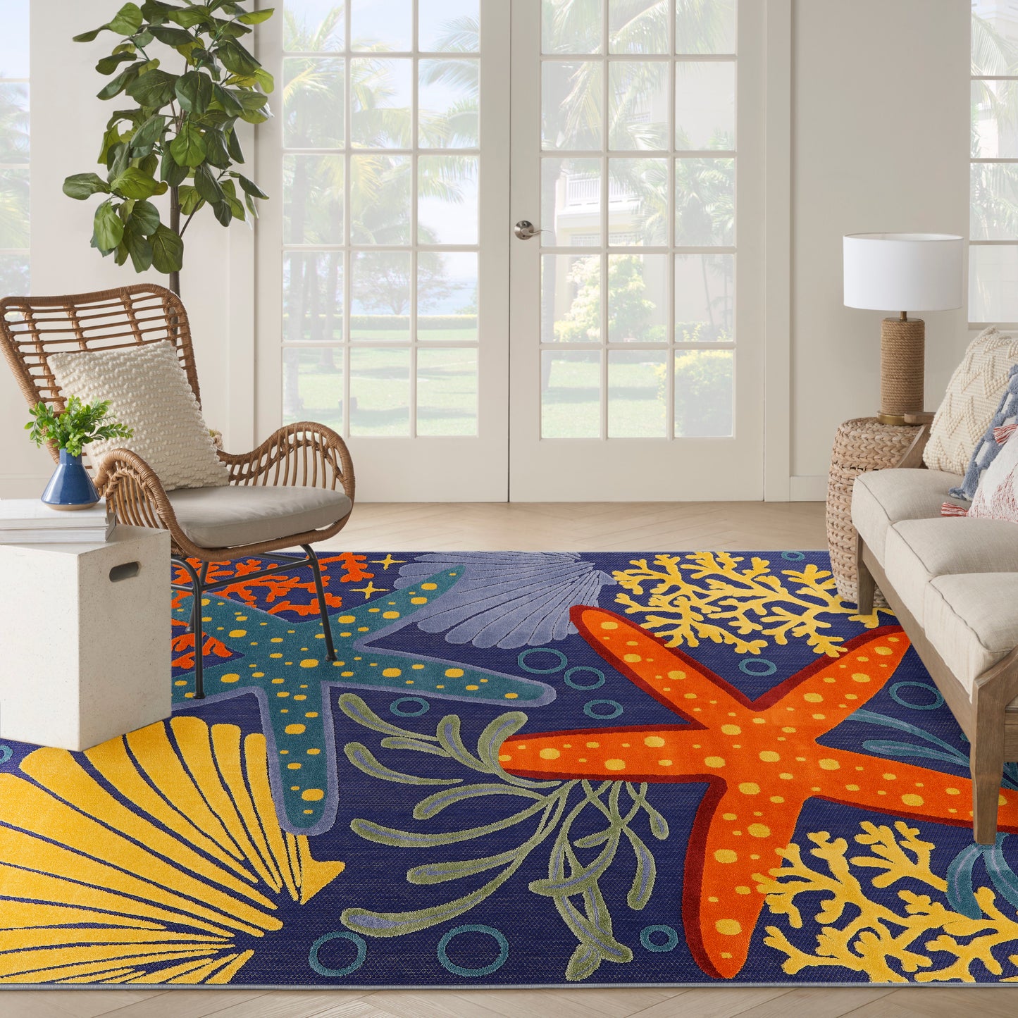Outdoor rug with a colorful coastal woven pattern featuring orange starfish and yellow coral on a navy background; rectangular, 9' x 12'.