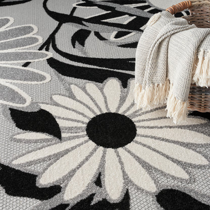 Woven gray rug featuring large white daisy shapes with black centers; beige fringed throw over a wicker basket.